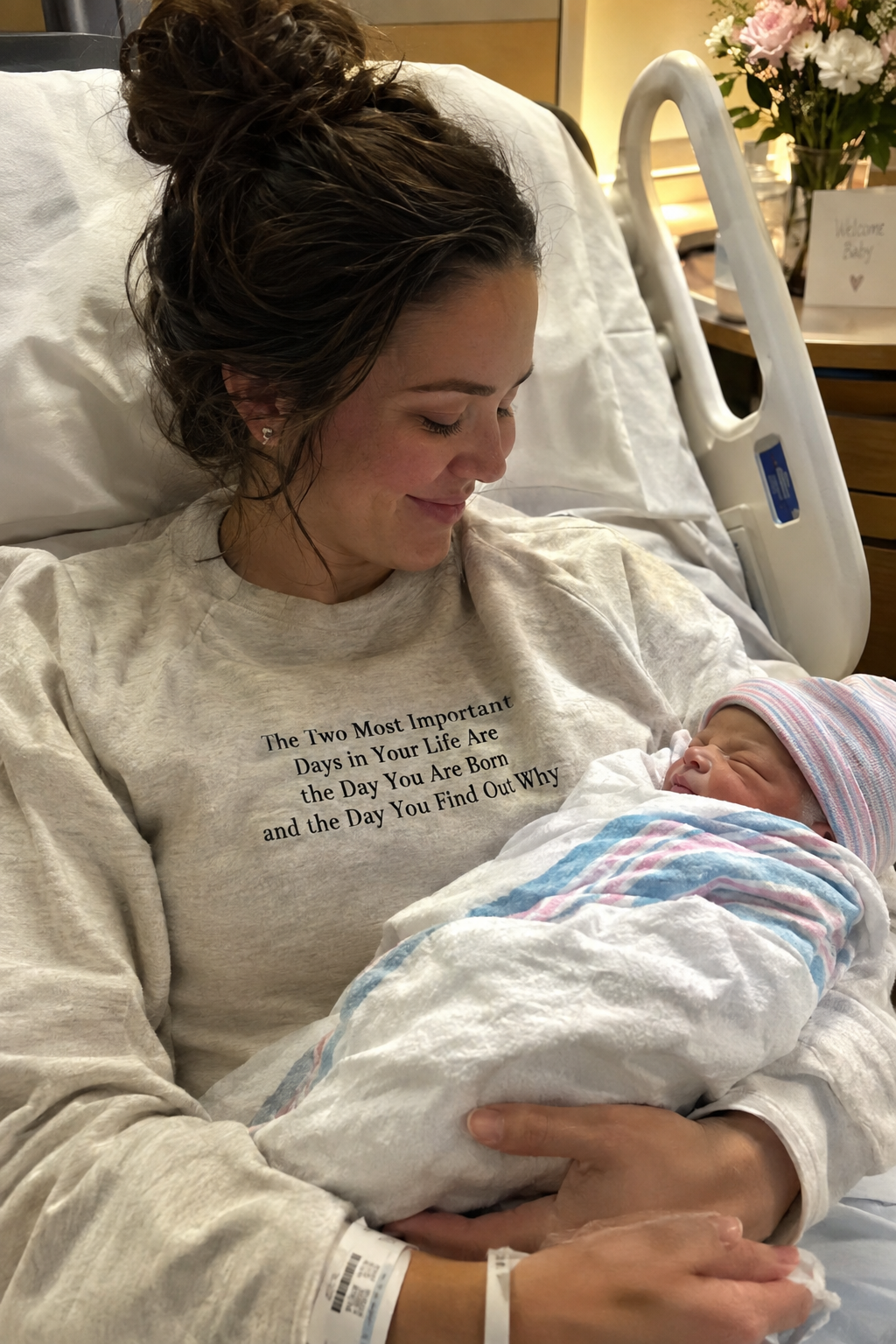 Mother in hospital bed holding newborn baby, wearing The Two Most Important Days crewneck